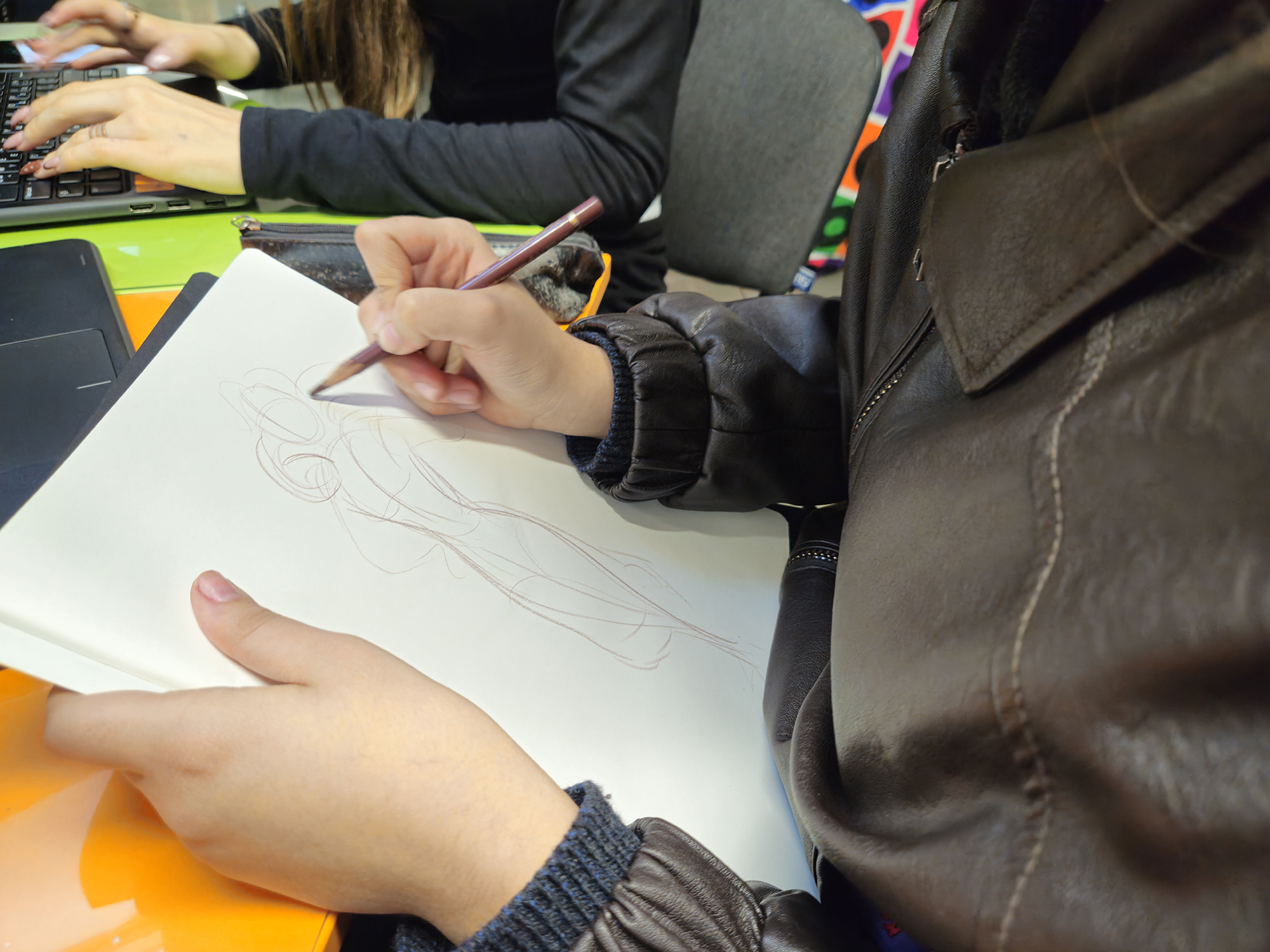 Hands sketching in sketchbook and laptop work during the workshop